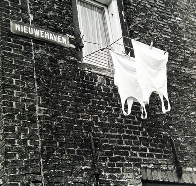 Bakstenen zijde van een huis waar een wasrekje uit het raam hangt met twee hemden er aan.